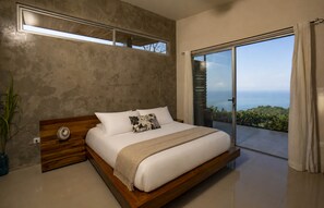 Ein modernes Schlafzimmer mit einem großen Bett, Blick ins Freie und einer Betonwand.