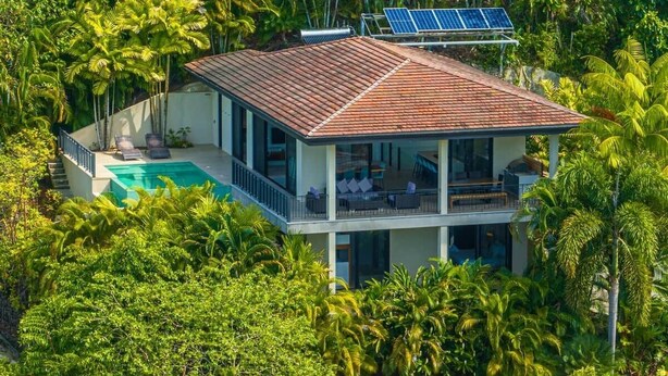 Una casa de dues plantes amb piscina, envoltada d'una vegetació tropical densa.