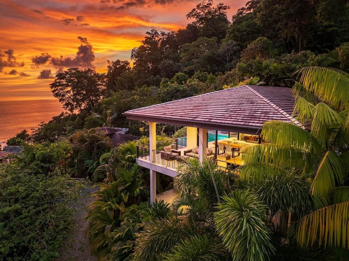 Una casa de dos pisos con un balcón que da a un paisaje exuberante y una masa de agua.