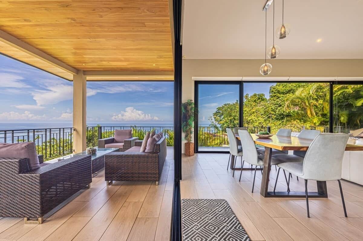A modern outdoor living area with a wooden ceiling, wicker furniture, and a dining table with chairs.