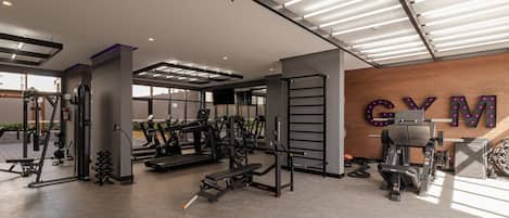 A gym with various exercise equipment, a wall-mounted TV, and a large 'GYM' sign.