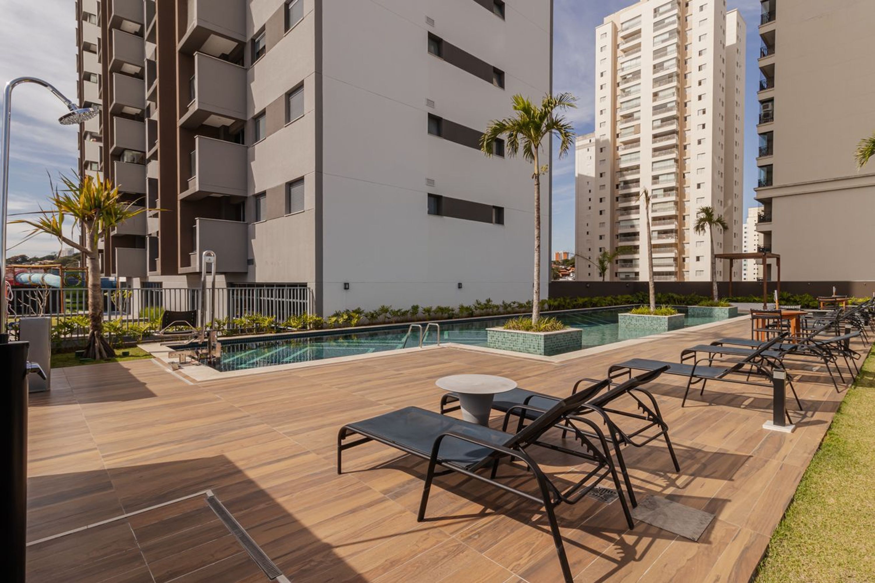 A rooftop pool area with lounge chairs and a small table, surrounded by a modern building with balconies.
