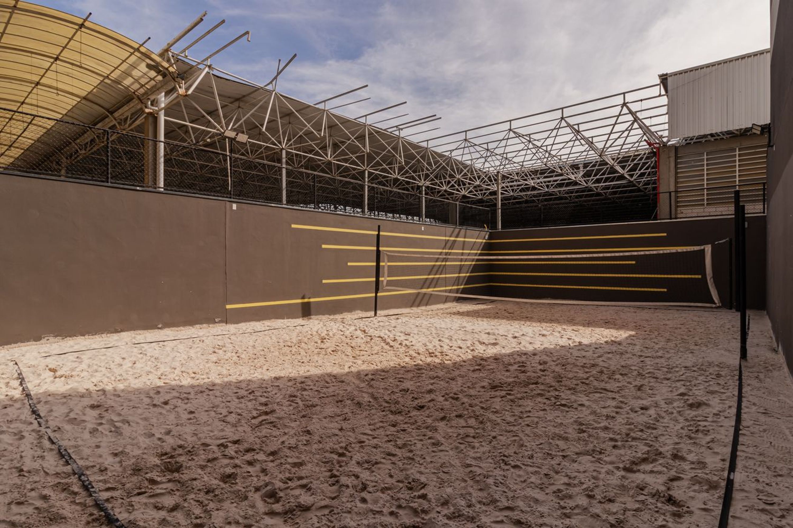 An indoor sandy area with a metal roof structure and a wall with yellow lines.