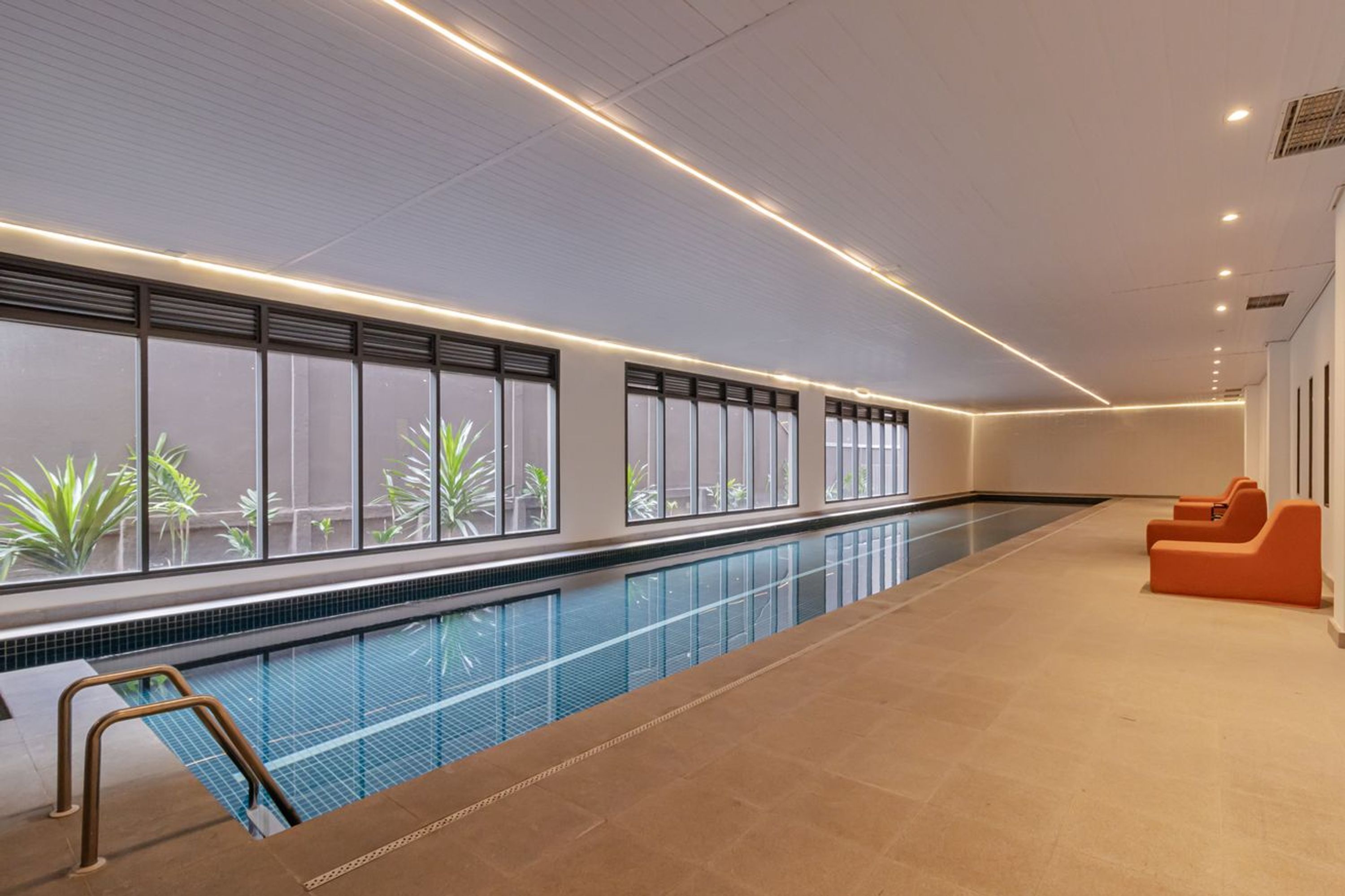 Piscina com vista para o verde do exterior, piso ladrilhado e áreas de estar em tons de laranja.