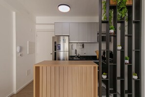 A modern kitchen with a built-in island, stainless steel appliances, and a black shelving unit with plants. - Apto com Piscina e Sauna Perto do Thermas do Vale (São José dos Campos)
