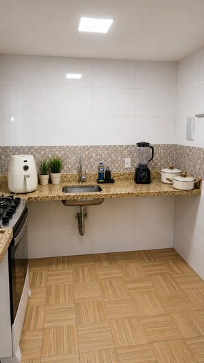 Una cocina con estufa a gas, un lavamanos, una licuadora y una planta en maceta.