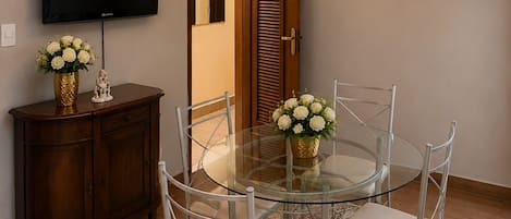 A dining area with a glass table, metal chairs, a wooden cabinet, a television, and a chandelier.
