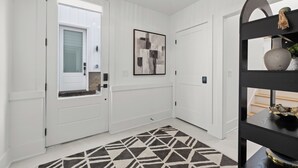 A hallway with white walls, a geometric patterned rug, and a framed abstract painting. - Velvet Note@ The New Cumberland Side B (Nashville)