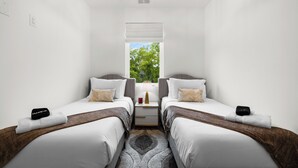 Une chambre d’hôtel avec deux lits simples, une table de chevet avec une lampe, une fenêtre donnant sur des arbres et un luminaire au plafond.