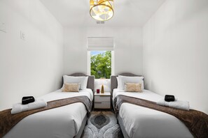 A hotel room with two single beds, a nightstand with a lamp, a window with a view of trees, and a ceiling light fixture. - Velvet Note@ The New Cumberland Side B (Nashville)