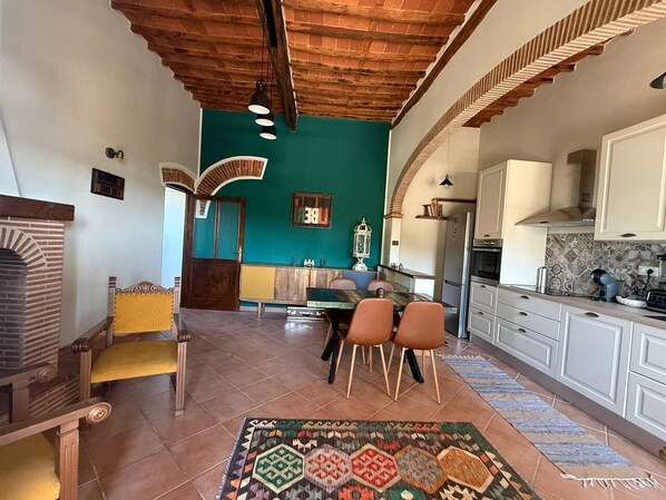 A kitchen with white cabinets, a dining area with a table and chairs, and a patterned rug on the floor.