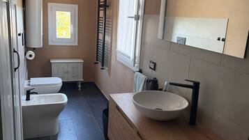 A modern bathroom with a toilet, bidet, and sink. There is a window with a view of the outside, a towel rack, and a mirror above the sink.