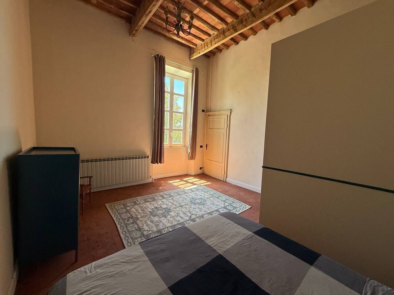 Ein Zimmer mit einem Bett, einem Heizkörper, einem Fenster mit Vorhängen und einer Tür.