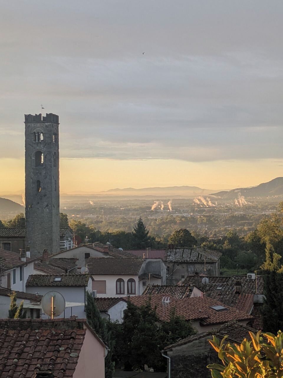 Ein Turm mit einer Uhr, umgeben von traditionellen Gebäuden mit roten Ziegeldächern.