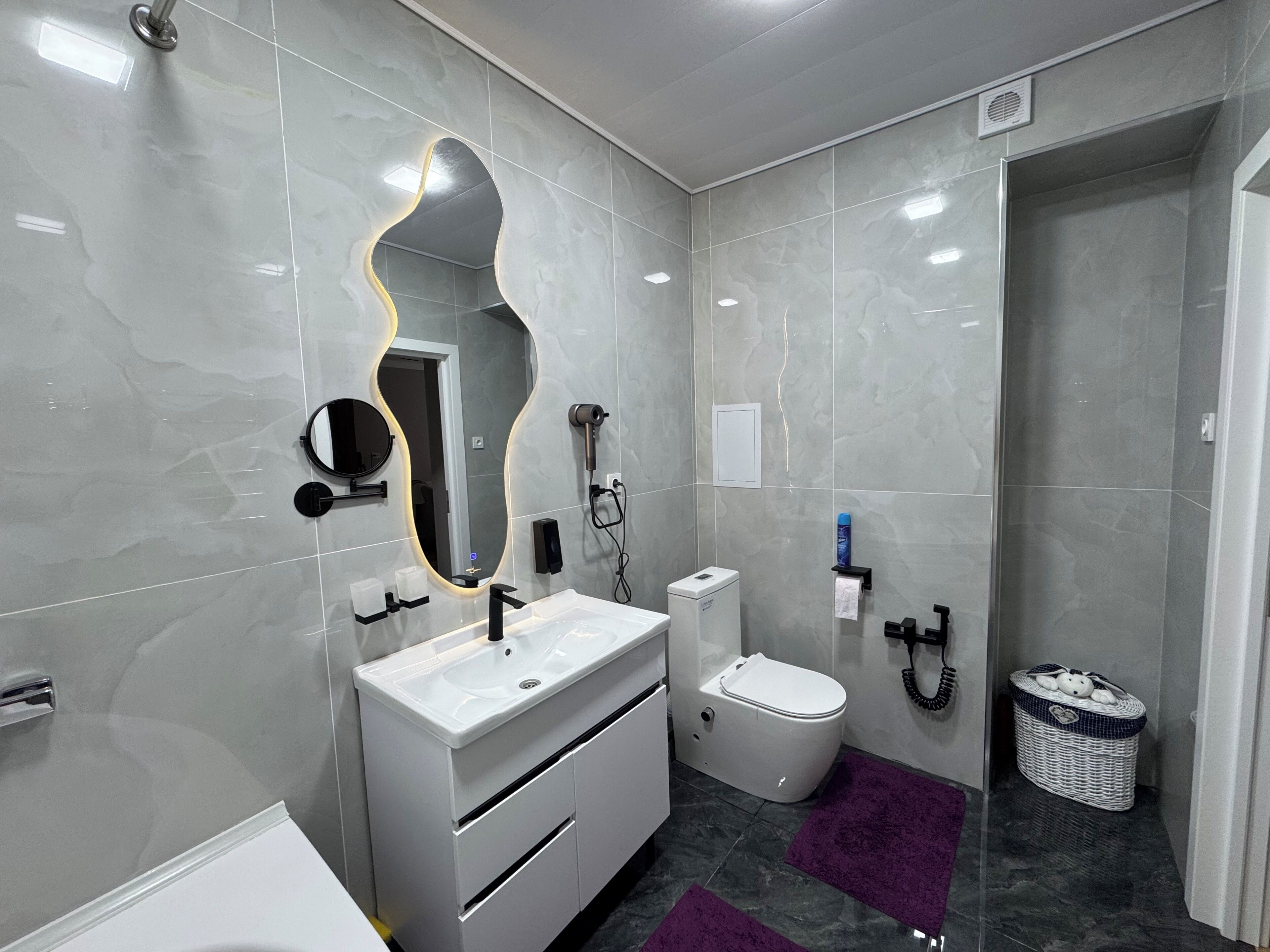 Un bany modern amb un lavabo blanc, un vàter, un mirall amb una estructura original i una zona de dutxa.