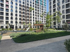 Ein Spielplatz mit Rutschen und Schaukeln, umgeben von einem gepflegten Rasen und einem gepflasterten Weg.