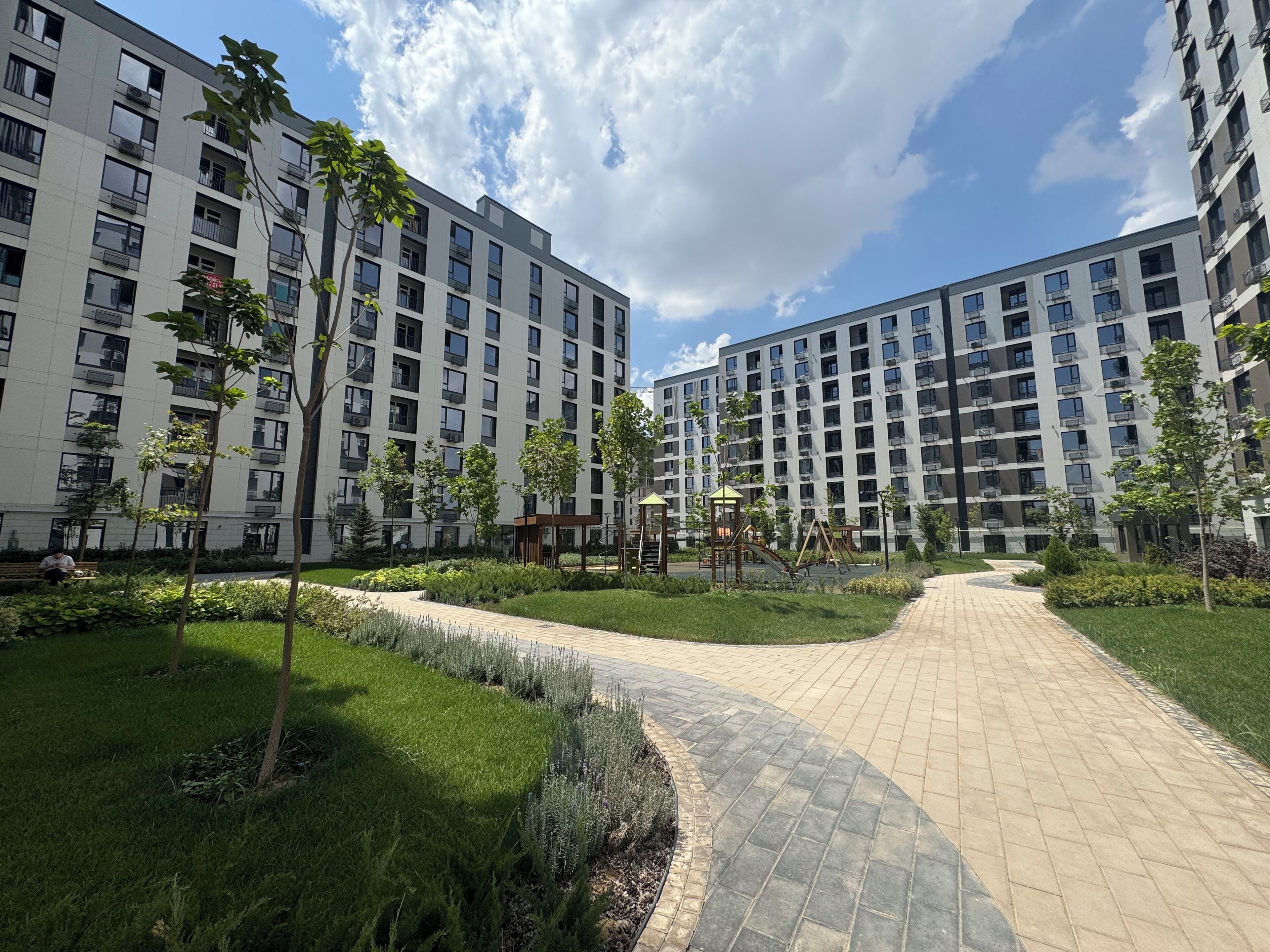 Um edifício residencial com vários andares, um caminho pavimentado e áreas verdes.