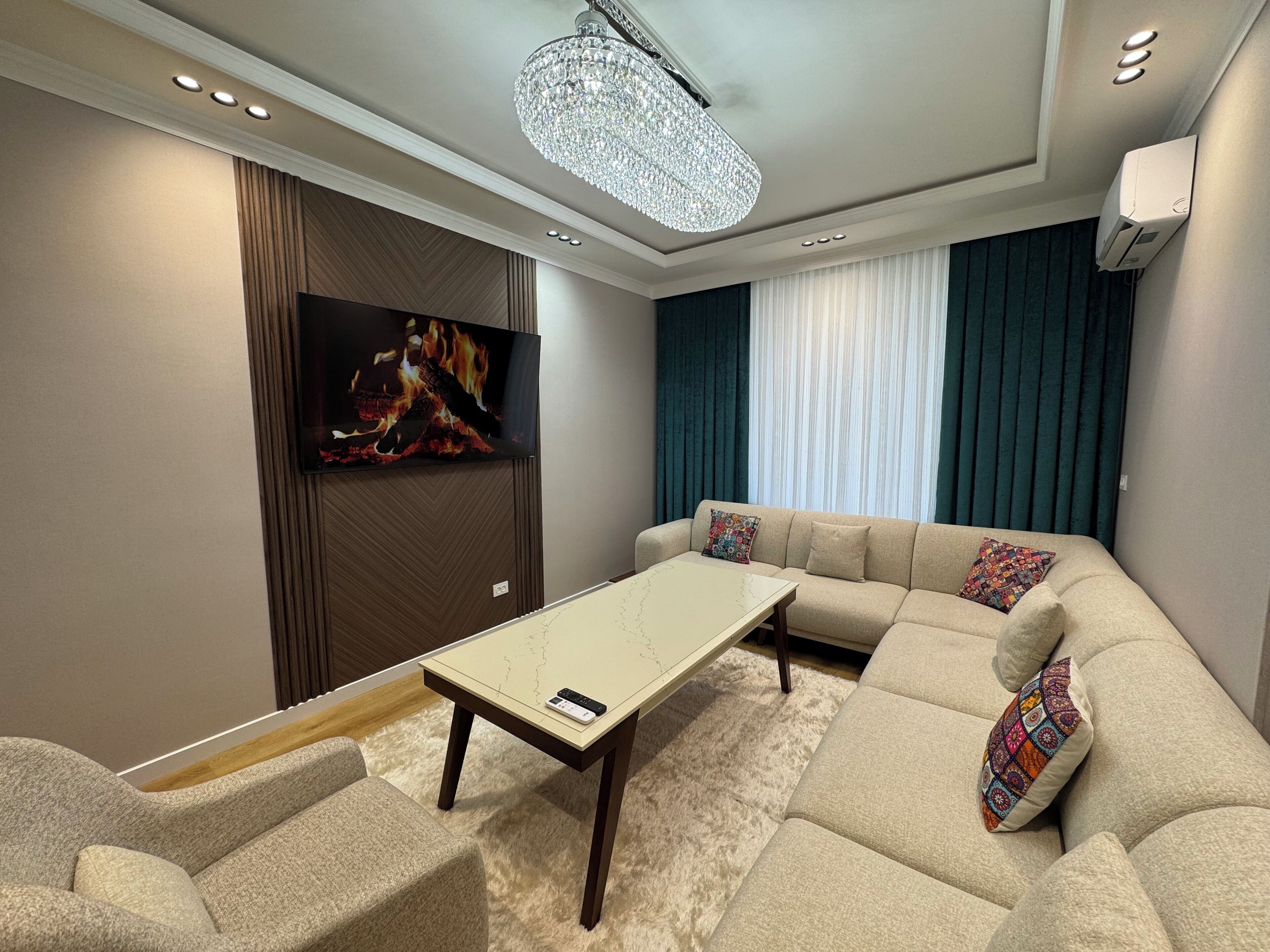 Un salon moderne avec un canapé d’angle, un téléviseur à écran plat, une table basse et un lustre.