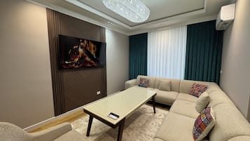 Un salon moderne avec un canapé d’angle, un téléviseur à écran plat, une table basse et un lustre.