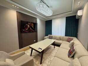 Ein modernes Wohnzimmer mit einer Eckcouch, einem Flachbildfernseher, einem Couchtisch und einer Pendelleuchte.