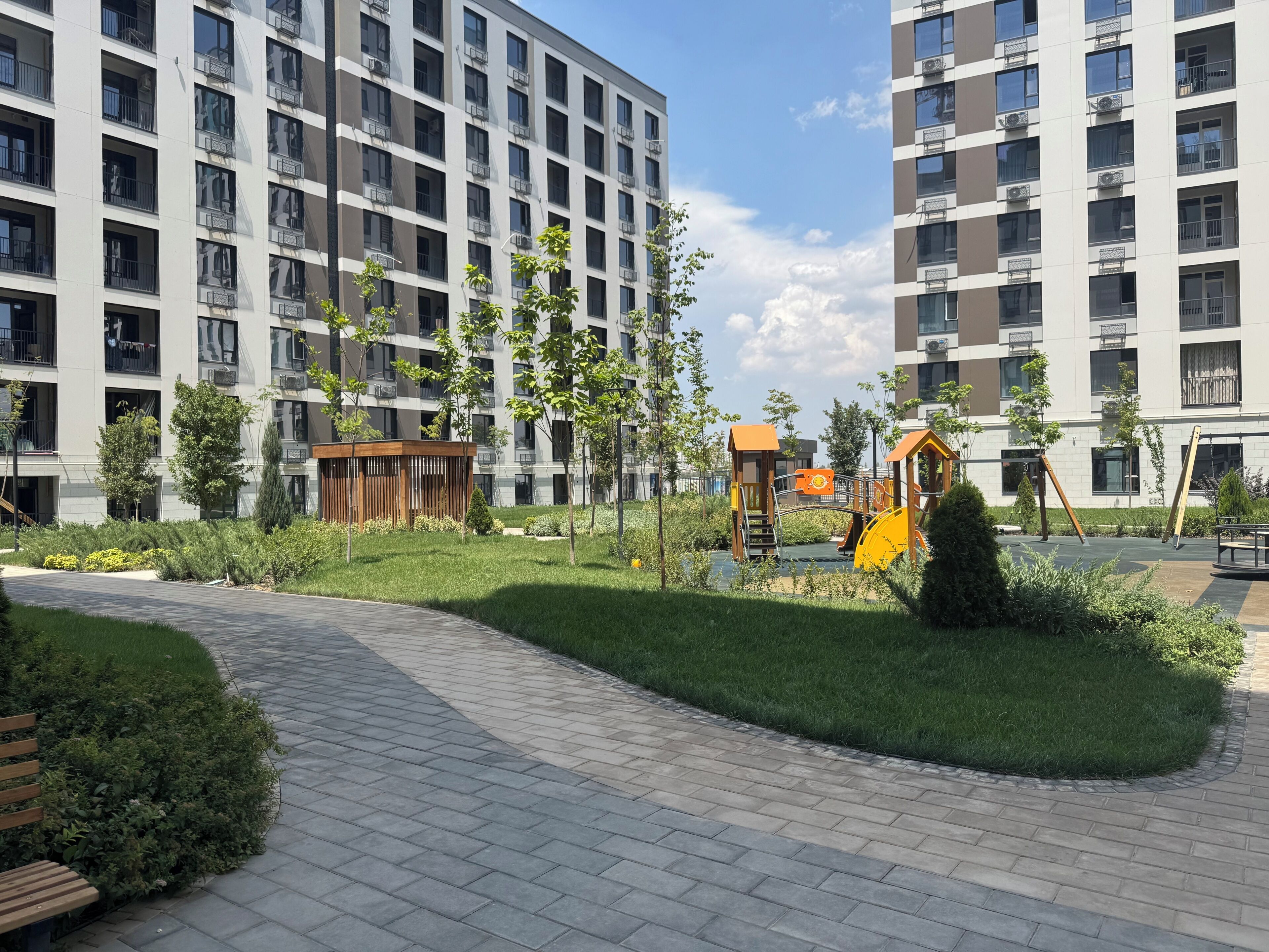 Ein Wohngebäude mit mehreren Balkonen, einem Spielplatz und einem gepflasterten Weg.