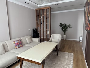 Ein modernes Wohnzimmer mit einer Couch, einem Couchtisch, einem Holzregal, einer Topfpflanze und einem Fernseher.