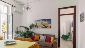 A living room with a sofa, a dining table, and a painting of a building. - Casa Ninetta - Terrace near Central Station (Palermo)