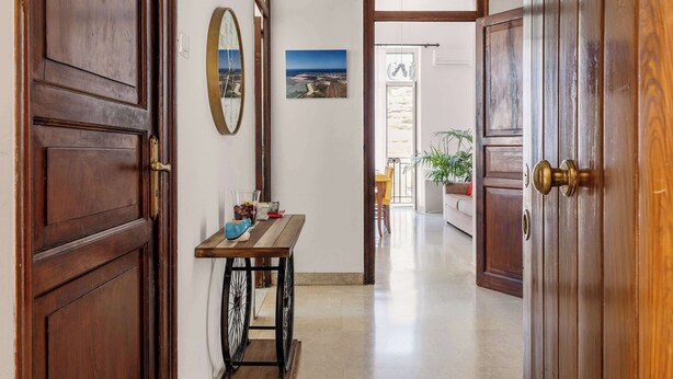 A hallway with wooden doors, a table with a vase and a glass, and a painting on the wall. - Casa Ninetta - Terrace near Central Station (Palermo)