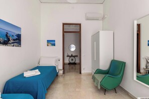Une chambre avec deux lits, un fauteuil vert, une armoire et un miroir fixé au mur.