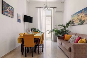 A dining area with a table and chairs, a television, and a painting on the wall. - Casa Ninetta - Terrace near Central Station (Palermo)