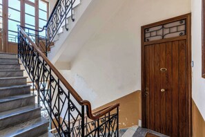 Un escalier doté d’une main courante en bois et de balustrades en métal noir, menant à une porte ornée d’un panneau décoratif.