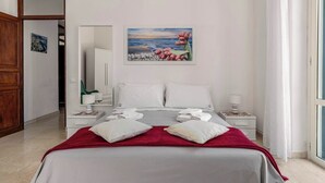 A hotel room with a bed, two bedside tables, a nightstand, a painting, and a view of the sea. - Casa Ninetta - Terrace near Central Station (Palermo)
