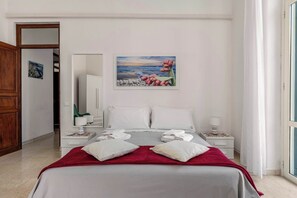 Ein Hotelzimmer mit Bett, zwei Nachttischen, einem Wandbild und Meerblick.