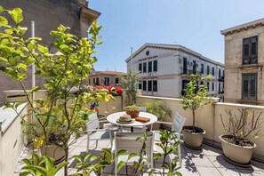 A terrace with outdoor seating, potted plants, and a view of historic buildings.
