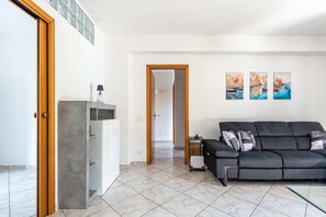 A living room with a grey sofa, a coffee table, and a door leading to another room. - Spacious Apartment close to the Beach-Isola Summer (Isola delle Femmine)
