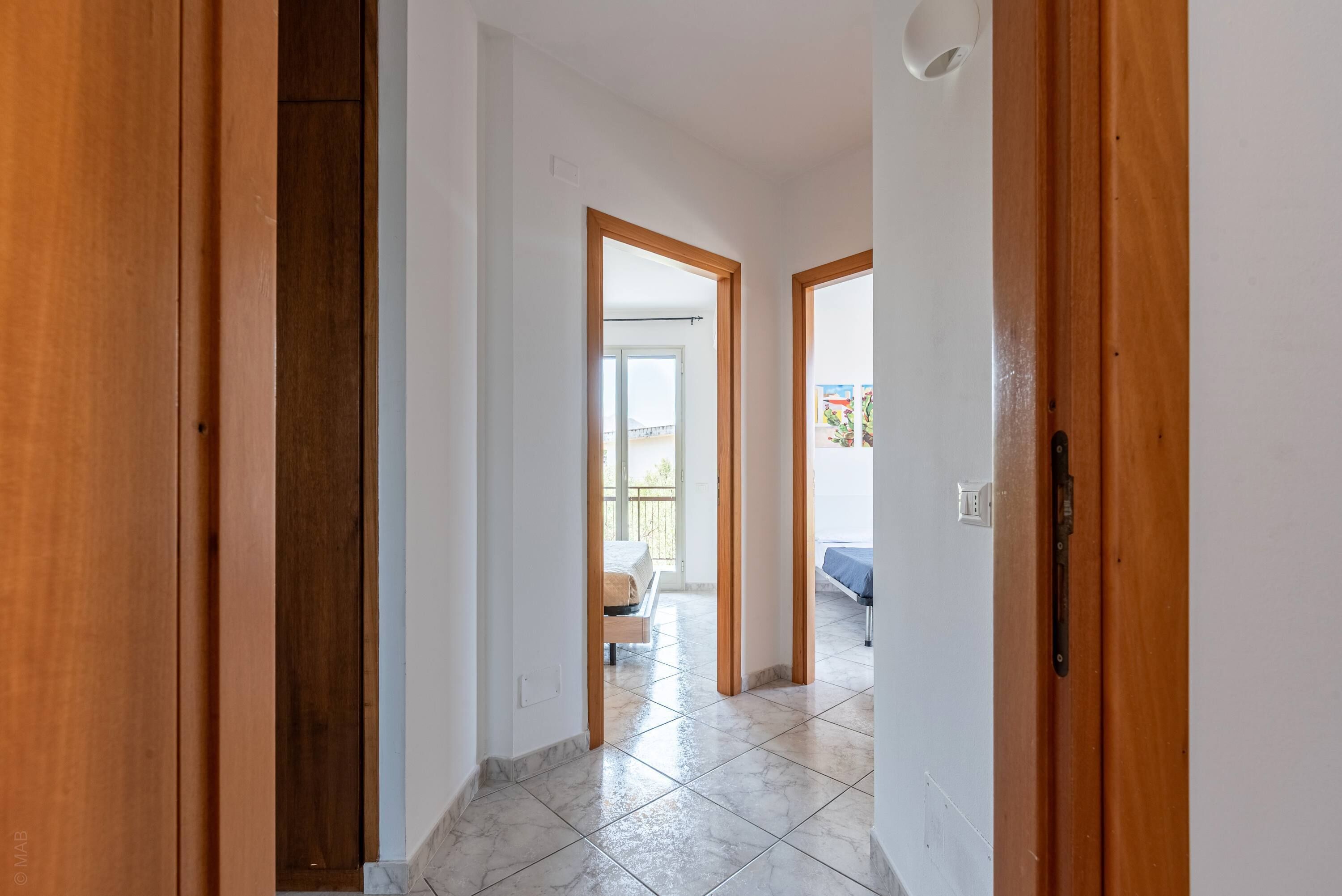 A hallway with wooden doors leading to a room with a bed and a balcony.