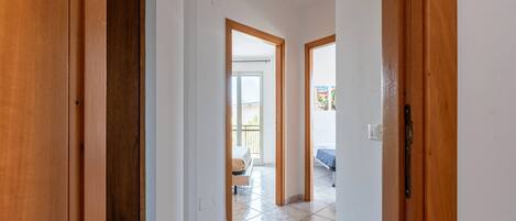 A hallway with wooden doors leading to a room with a bed and a balcony.