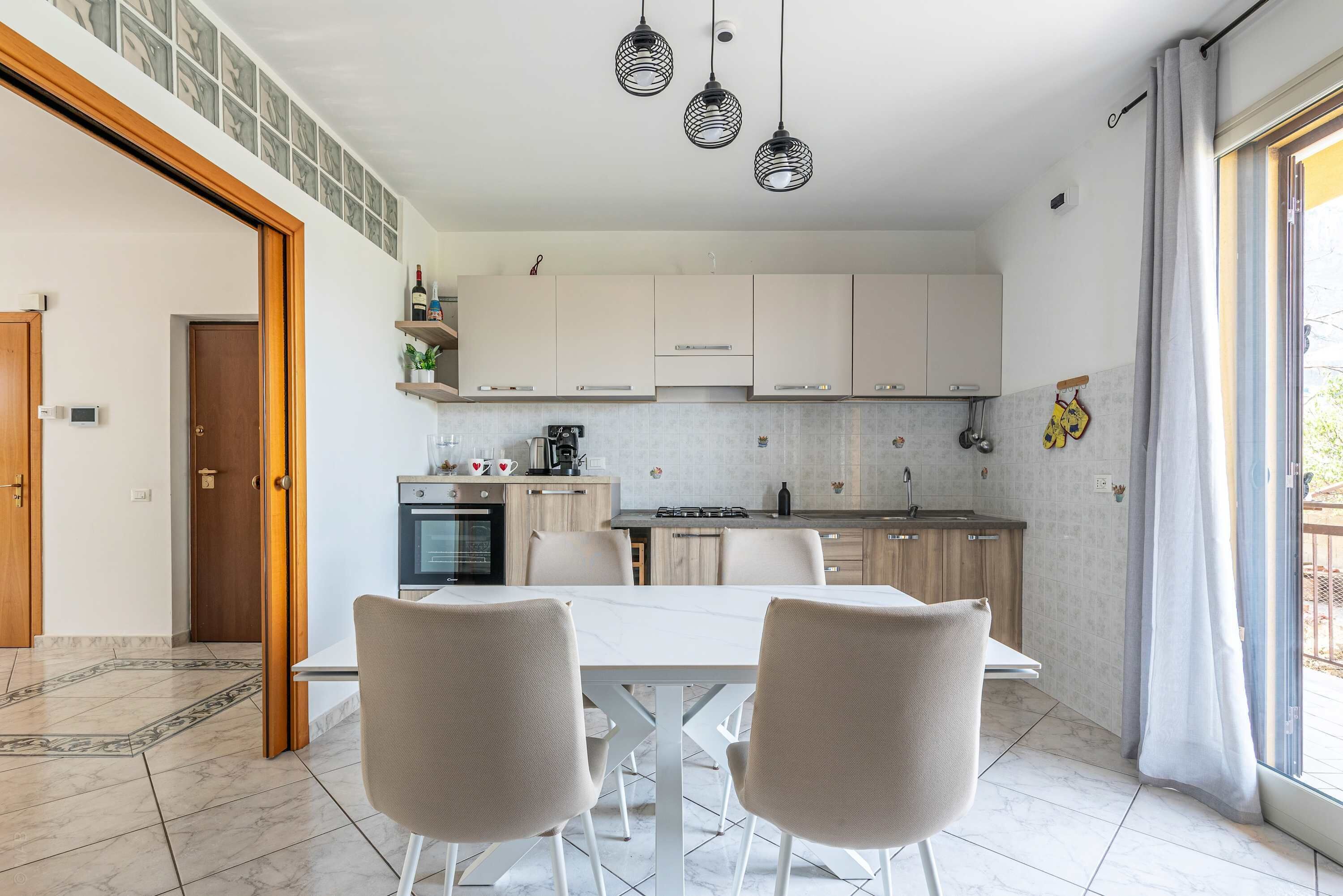 A modern kitchen with white cabinets, a dining table with two chairs, and pendant lighting.
