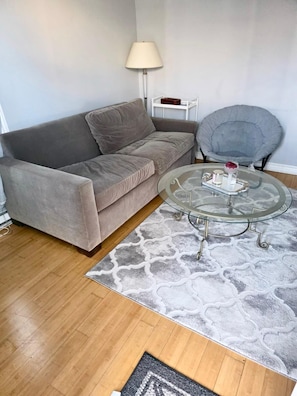 A living room with a grey sofa, a round glass coffee table, a grey armchair, and a patterned rug. - Charming 4½-room apartment near the Finnish Spa | Relaxation and business stays (Laval)