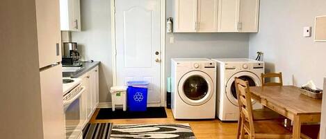 A compact kitchen with a refrigerator, washing machine, and a dining table with chairs.