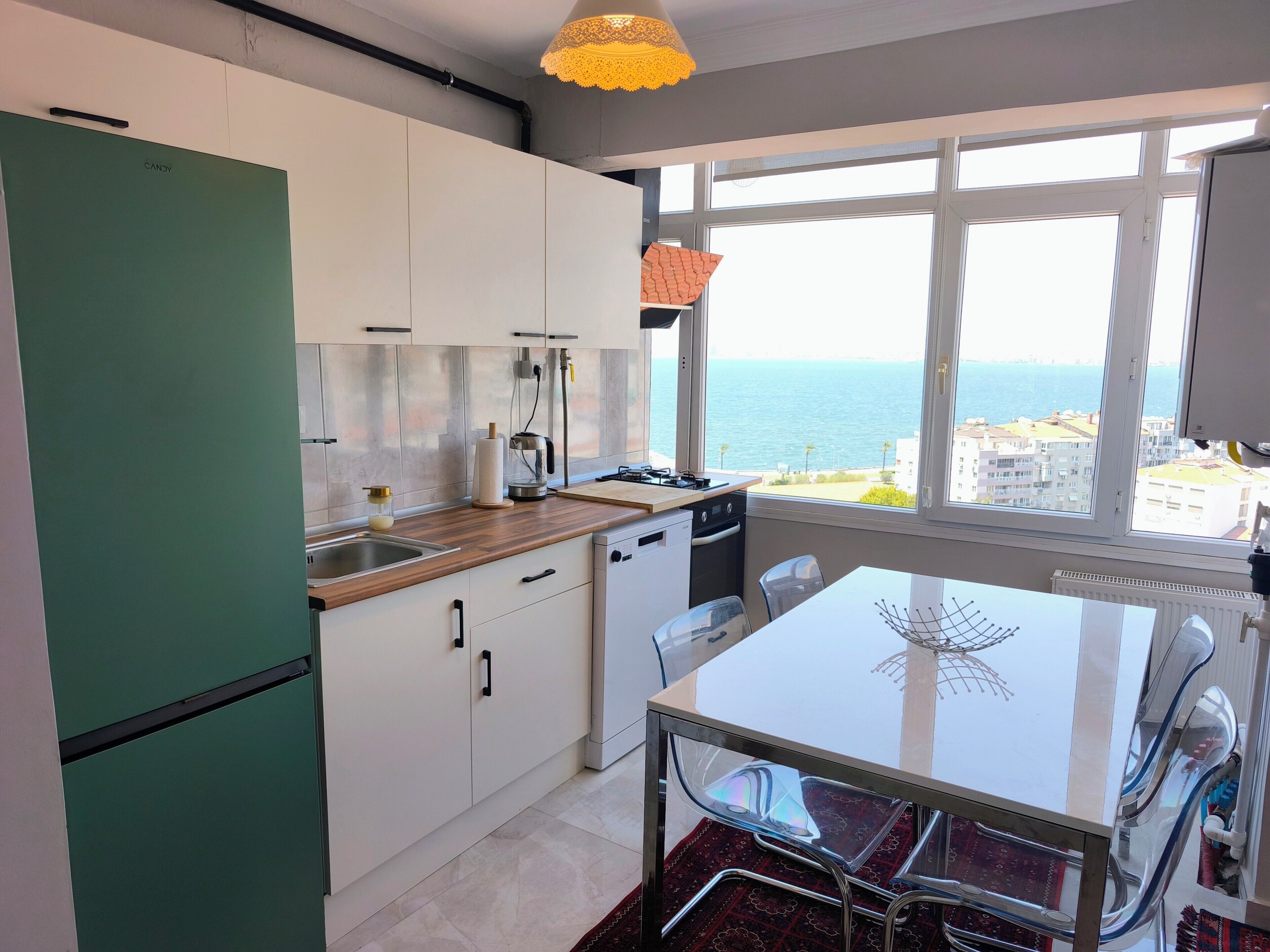 A modern kitchen with a view of the sea, a dining area with a glass table, and a green refrigerator.