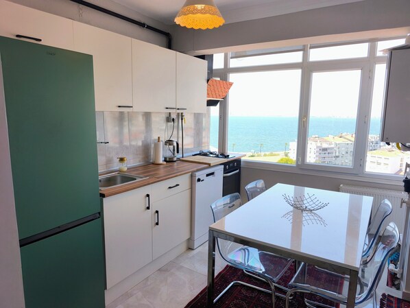 A modern kitchen with a view of the sea, a dining area with a glass table, and a green refrigerator.