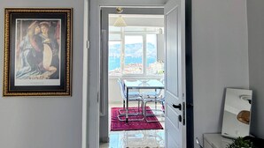 A hallway with a framed picture on the wall, a dining area with a table and chairs, and a view of the city through a window. - Renovated comfy apartment with unique sea view (Konak)