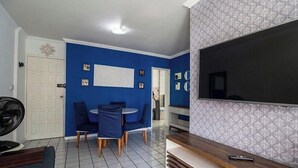 Ein Wohnzimmer mit blauer Wand, einem Flachbildfernseher, einer Essecke mit blauen Stühlen und einer weißen Tür.