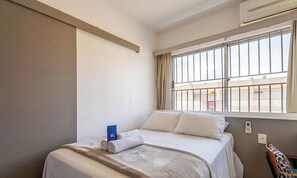 A hotel room with a bed, a window with curtains, a wall-mounted air conditioner, and a telephone. - Ground Fl. Apt. in Cond. in Asa Norte Sud0111 (Brasília)