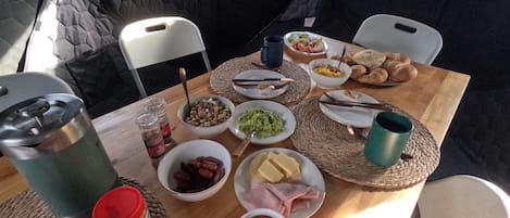 Una mesa con sillas y diversos alimentos dentro de una tienda de campaña.