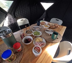 A meal setup inside a tent with a table, chairs, and various food items.