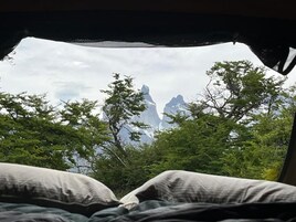 A bed with a view of mountains through trees.