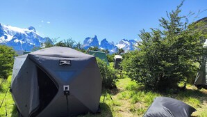A tent set up in a grassy area with a mountain view in the background. - Yellow Plum Camp Pehoé (Torres del Paine)