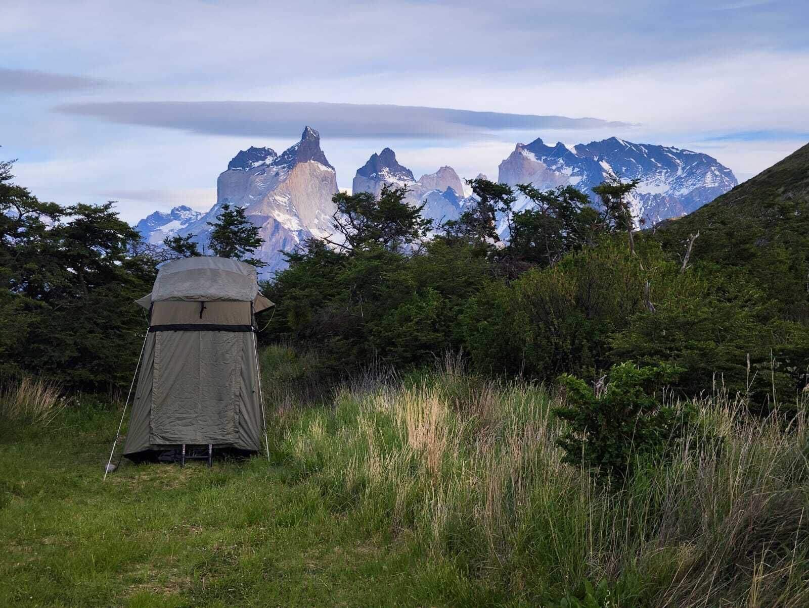 Uma tenda montada em um campo gramado, com montanhas ao fundo.